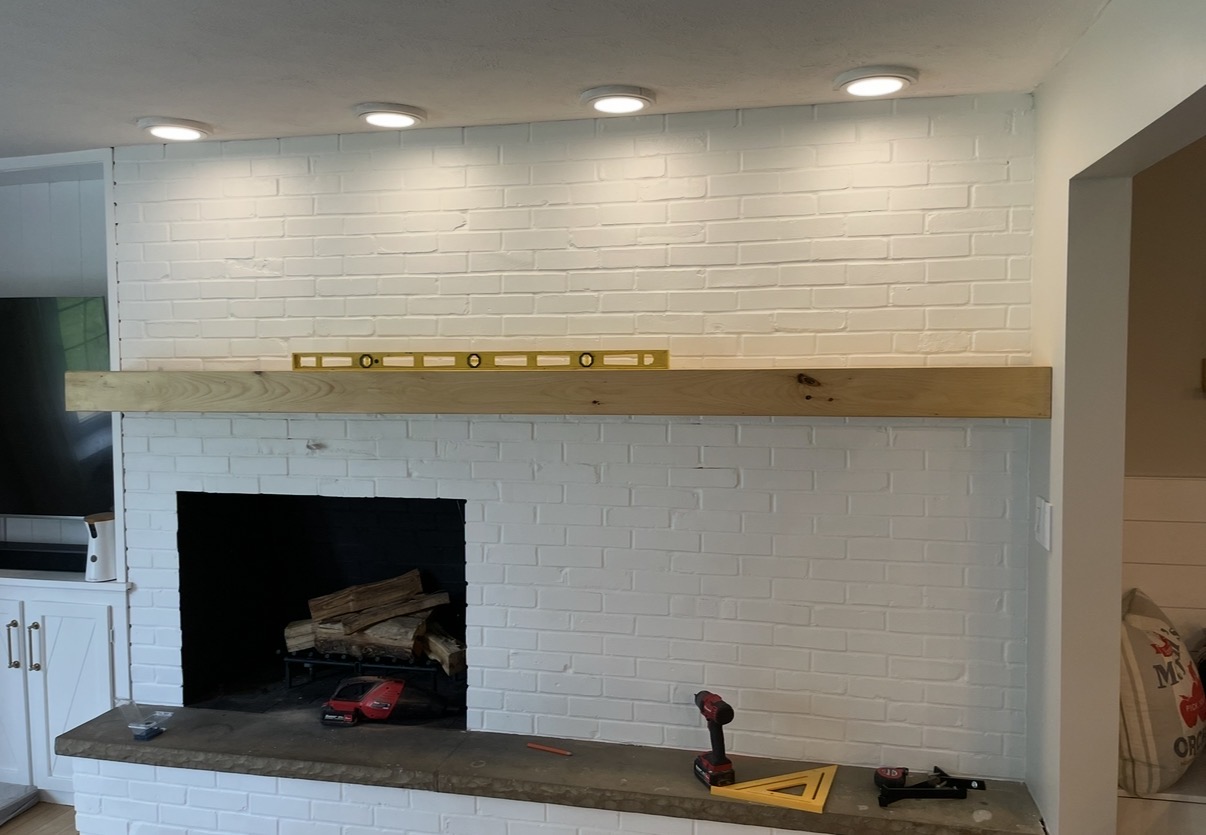White brick fireplace with a wood mantel and overhead lighting